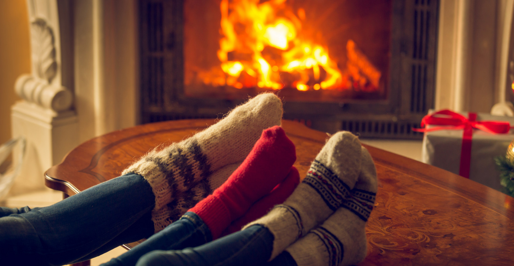 A couple wearing Christmas-colored socks resting their feet by the fireplace