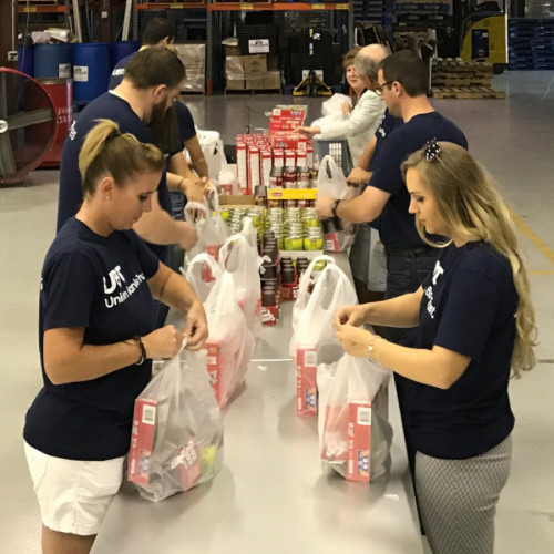 A row of UBT employees filling plastic sacks with food in a warehouse