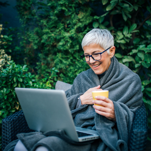 A woman in a blanket smiles as she looks at her laptop