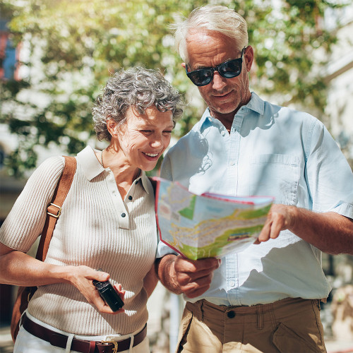 a mature couple stand together in a sunny place looking at a paper map