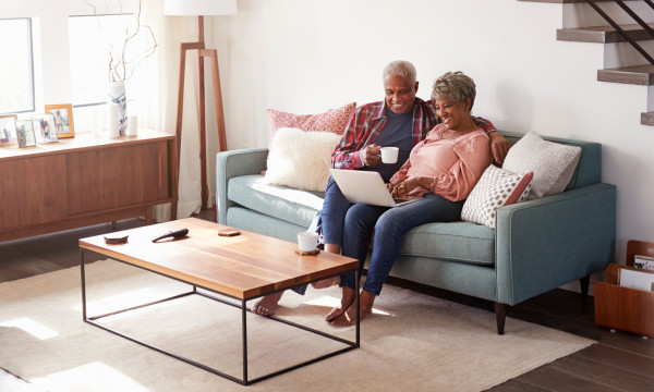 An elderly couple sitting on the couch looking at a laptop