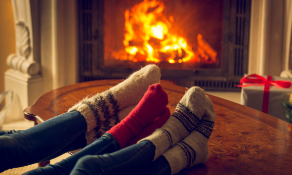 A couple wearing Christmas-colored socks resting their feet by the fireplace