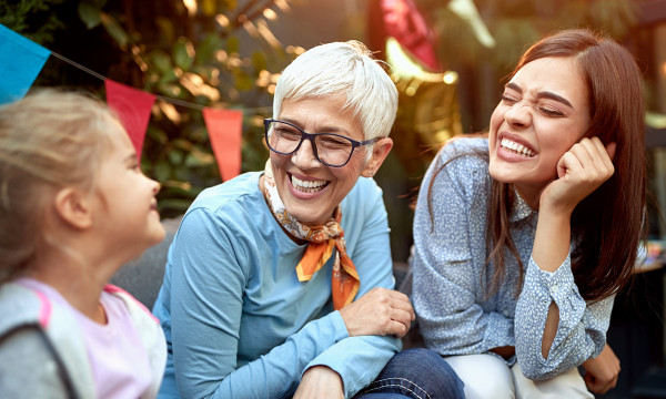An elderly lady, her daughter, and her granddaughter laughing in a backyard