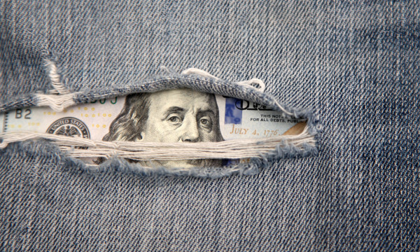 a hundred dollar bill peaks out of ripped jeans