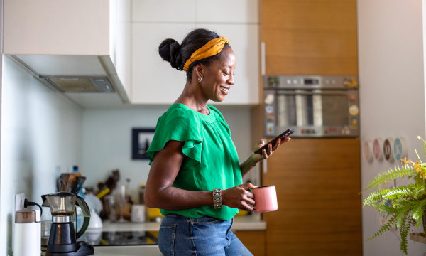 A woman holding a cup of coffee looking down at her phone