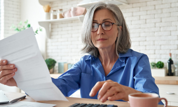 a mature woman sits at a table reading a piece of paper