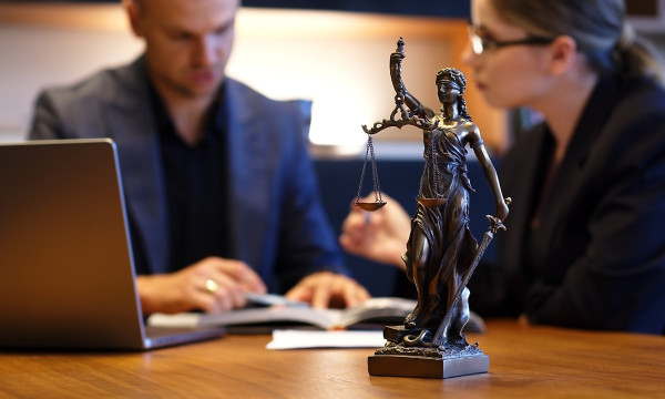 two people sit at a desk with a laptop and a statue